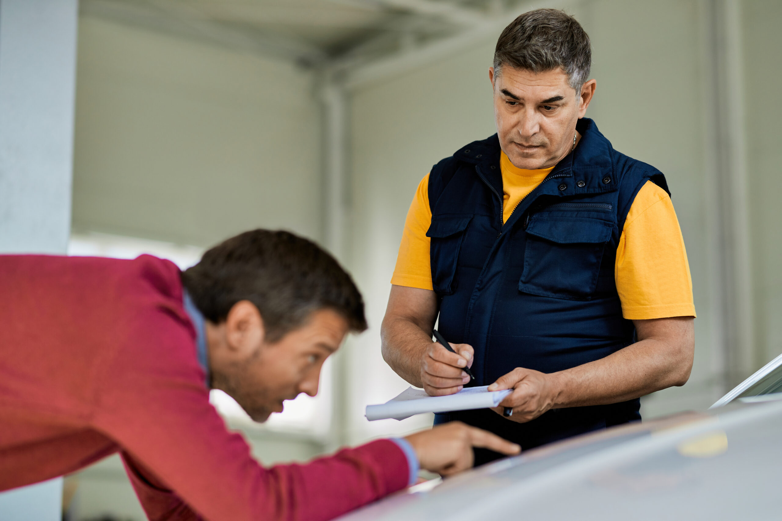 Auto mechanic taking notes while customer is showing his problem